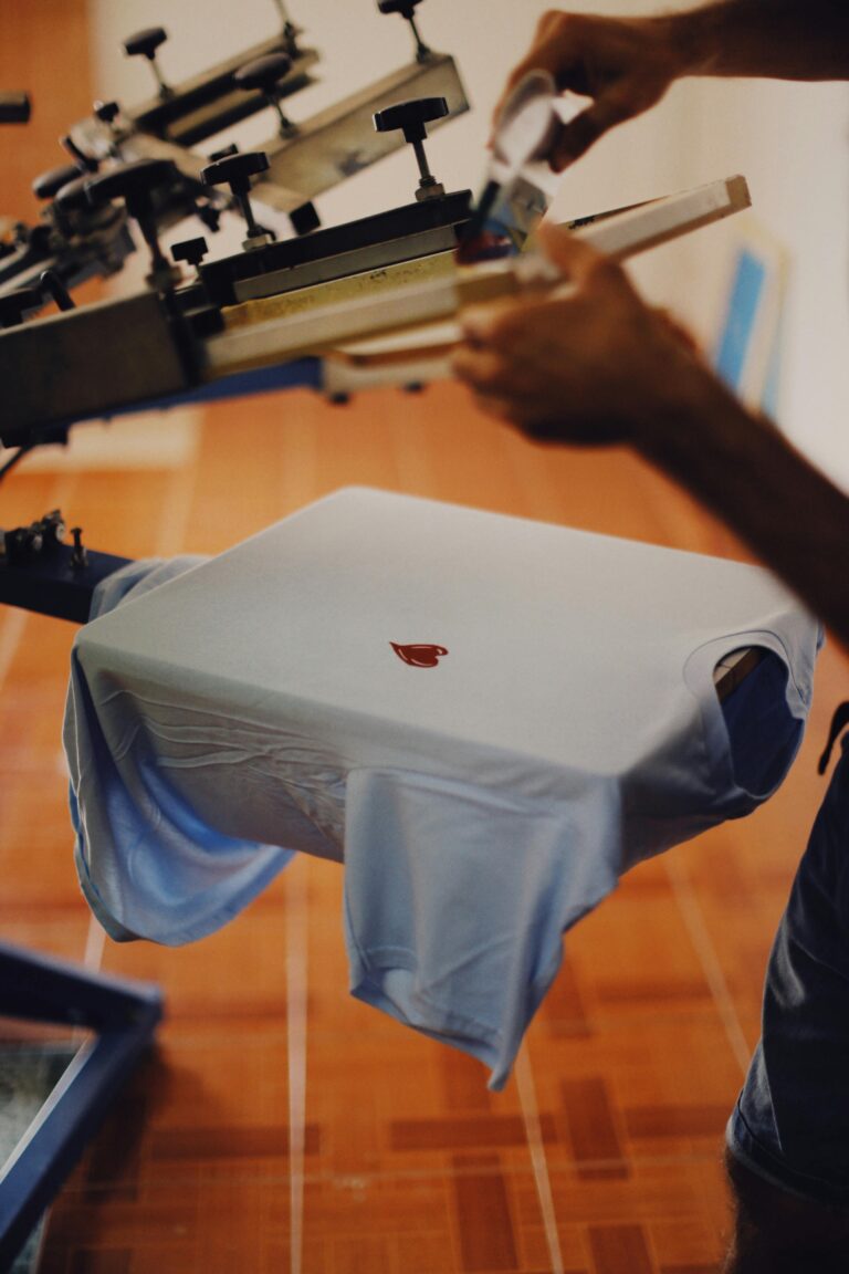 Close-up of a man using a T-shirt printing machine indoors. Marshe's signs and designs offers screen printing